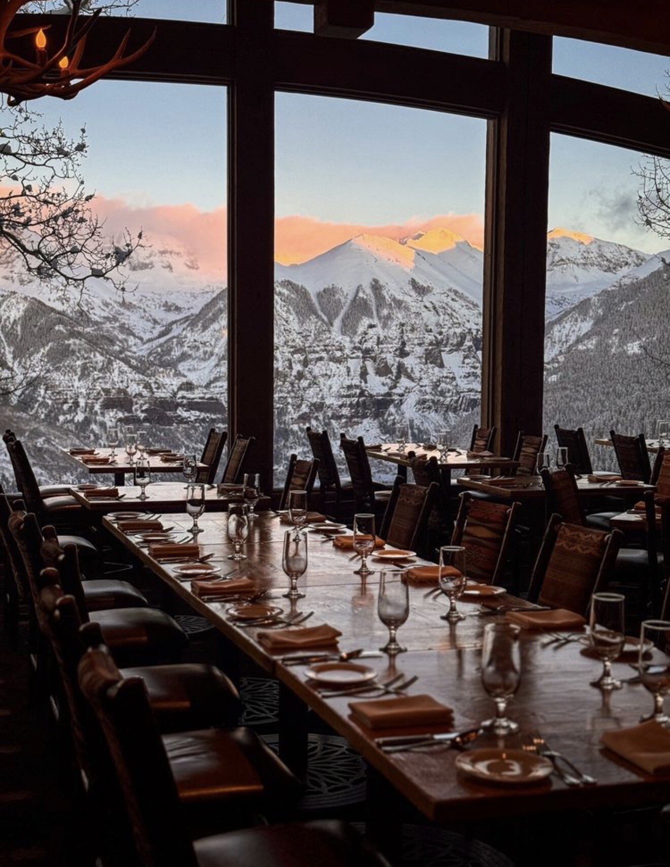 A long dining table set at Allred's, with alpenglow on the San Juan Mountains through floor-to-ceiling windows