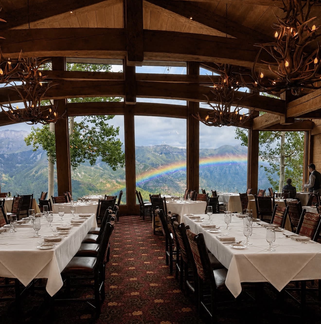 Allred's dining room set for service beneath antler chandeliers, with a rainbow arcing over the San Juan Mountains