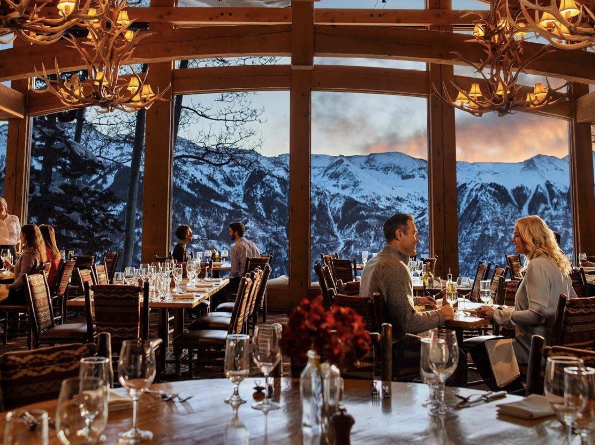 Guests dining at Allred's at golden hour, antler chandeliers above and the San Juan Mountains glowing through floor-to-ceiling windows