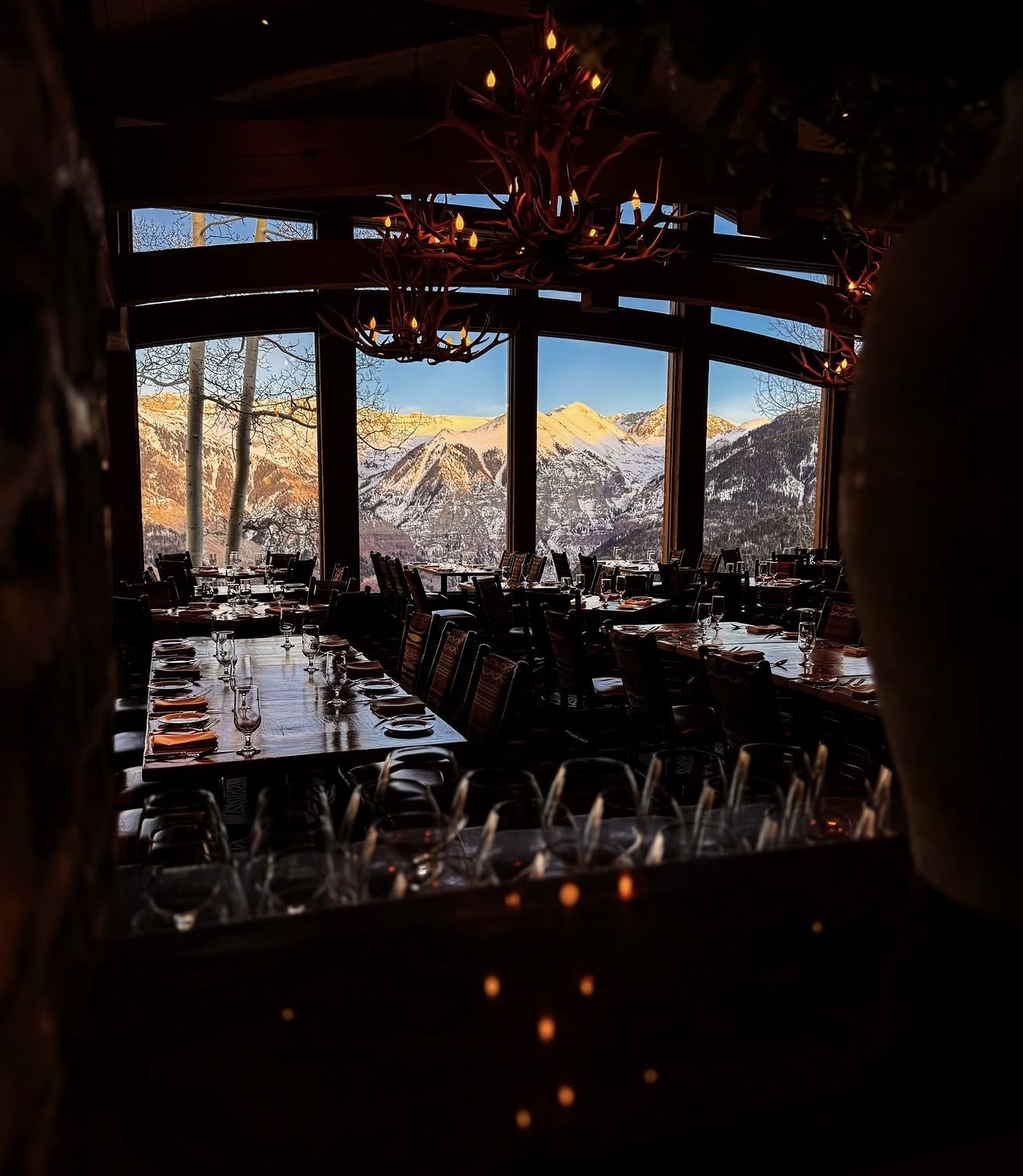 Allred's dining room at sunset, antler chandeliers above and alpenglow lighting the San Juan Mountains through floor-to-ceiling windows