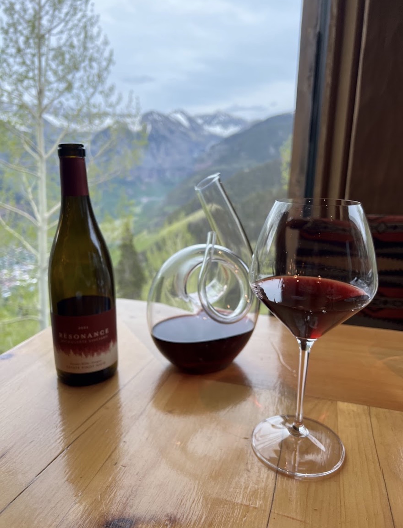 A bottle of Résonance Pinot Noir with a decanter and glass of red wine, overlooking the Telluride valley