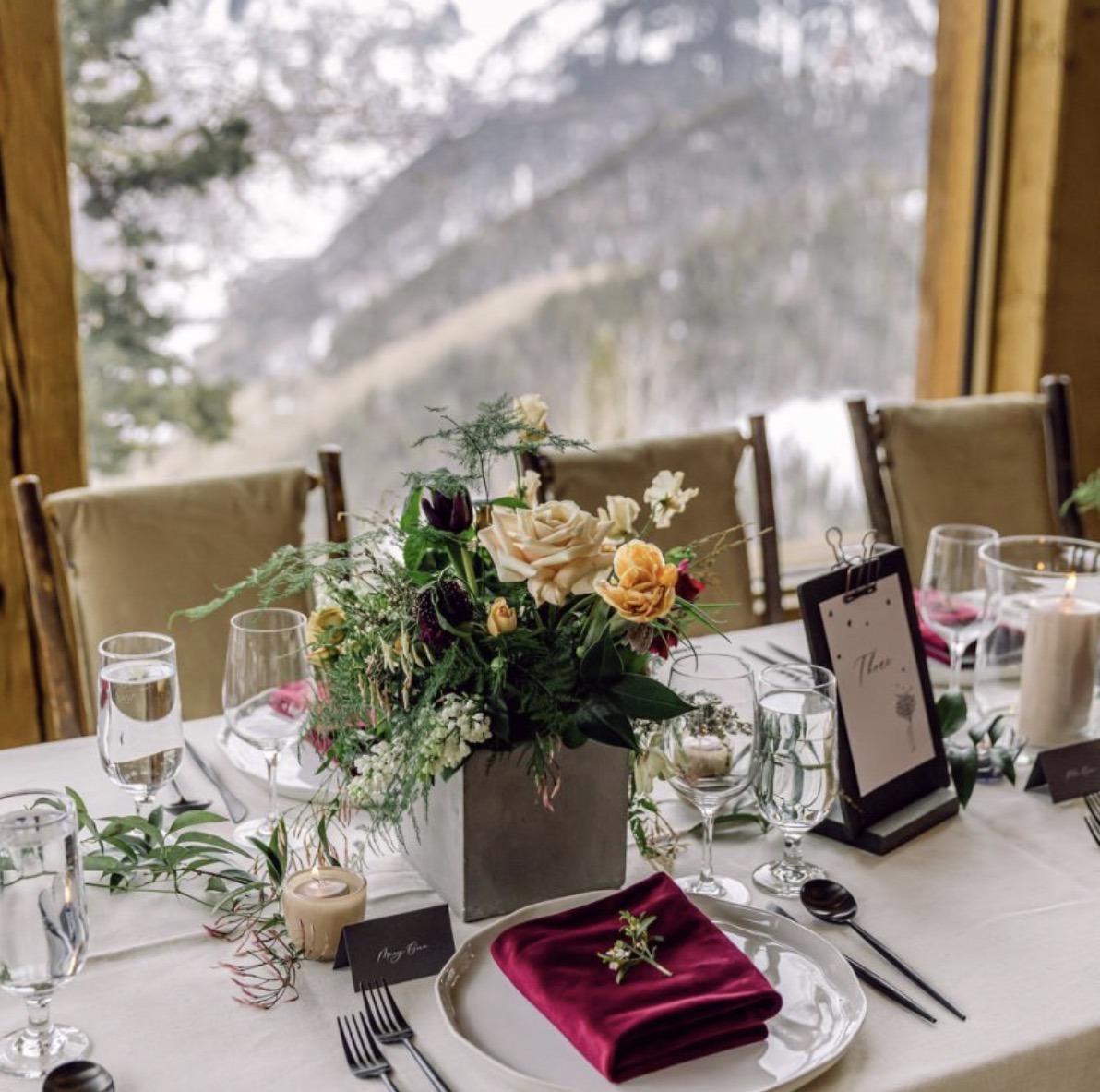 A wedding table setting at Allred's with a floral centerpiece, burgundy velvet napkin, and mountain views through the window