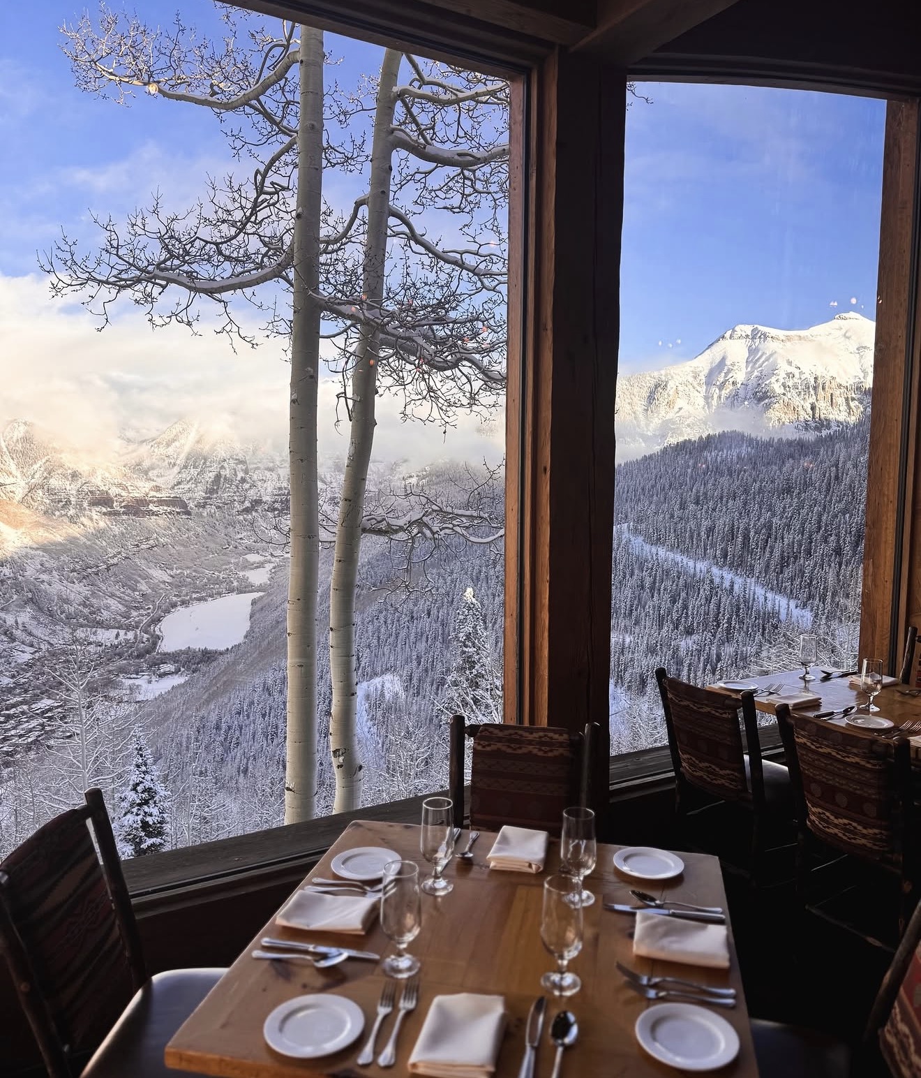 A window-side table set for dinner at Allred's in winter, framed by snow-dusted aspens and the San Juan Mountains